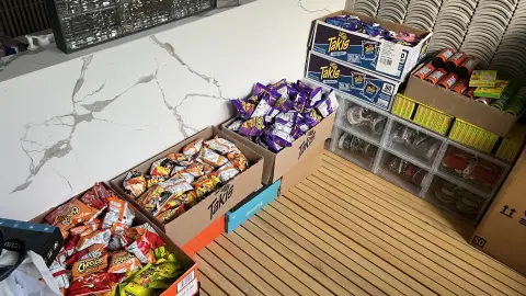 Open boxes of Cheetos, Takis and Sour Patch Kids lined up along a wall as working stock.